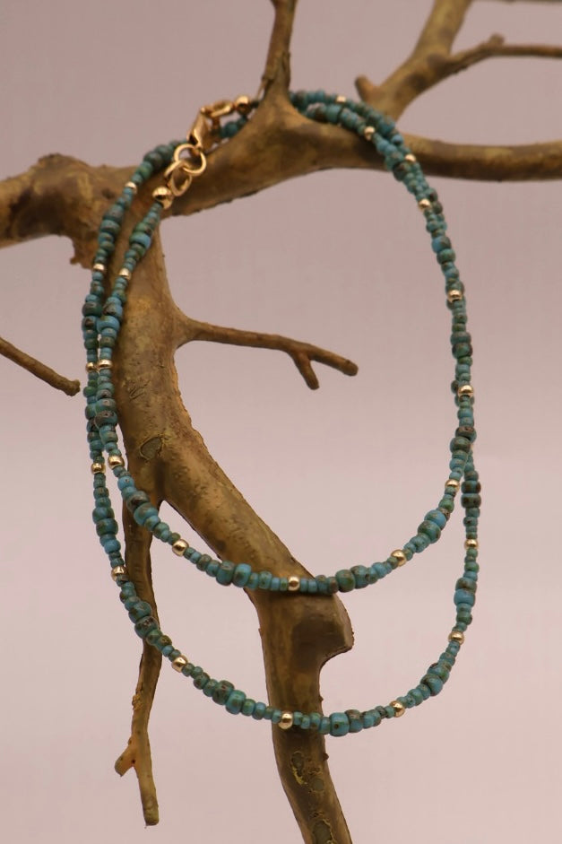 Green beaded necklace with gold accents on a branch against a neutral background