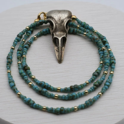 Necklace with blue beads and a silver skull pendant on a light gray background