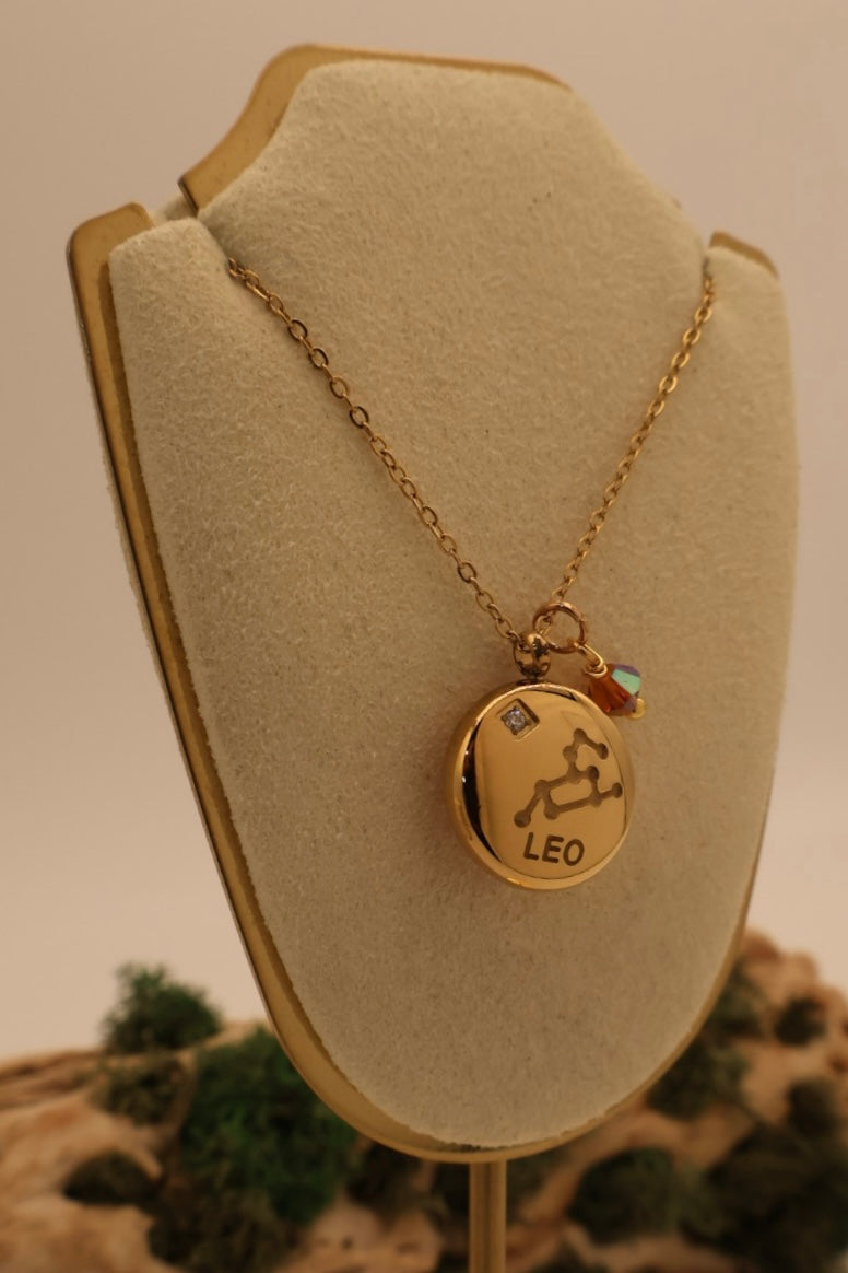 Gold necklace with a 'Leo' pendant on a beige display stand.