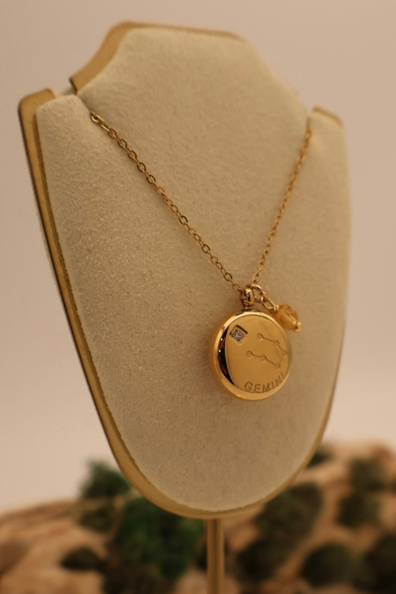 Gold necklace with a round pendant on a beige display stand.