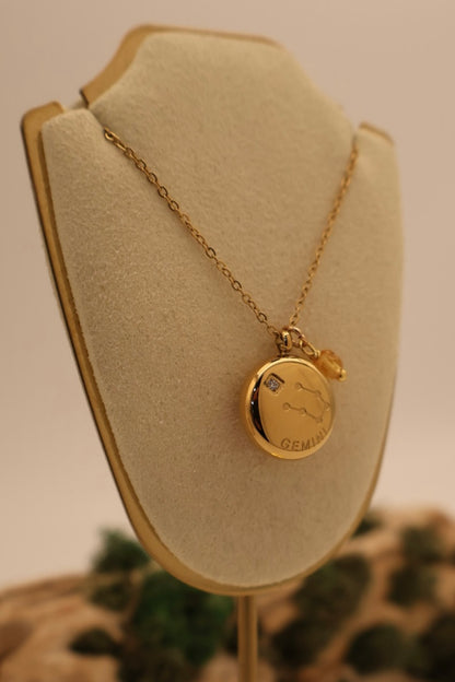 Gold necklace with a round pendant on a beige display stand.
