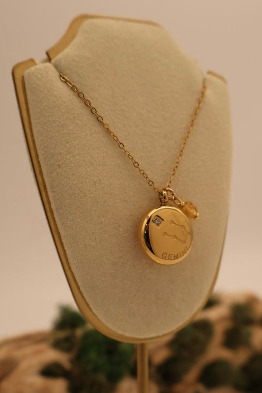 Gold necklace with a round pendant on a beige display stand.