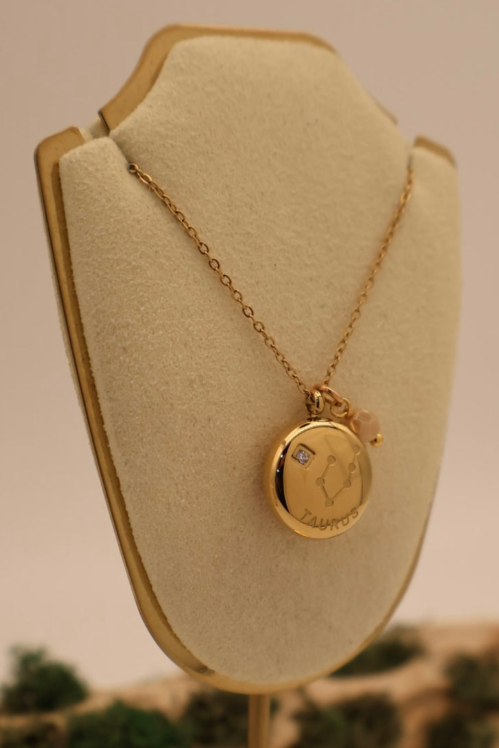 Gold necklace with a pendant on a beige display stand.