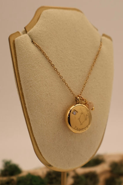 Gold necklace with a pendant on a beige display stand.