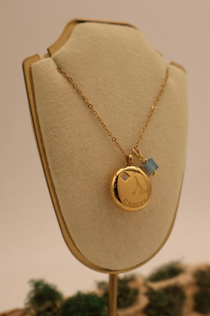 Gold necklace with a pendant on a beige display stand against a neutral background