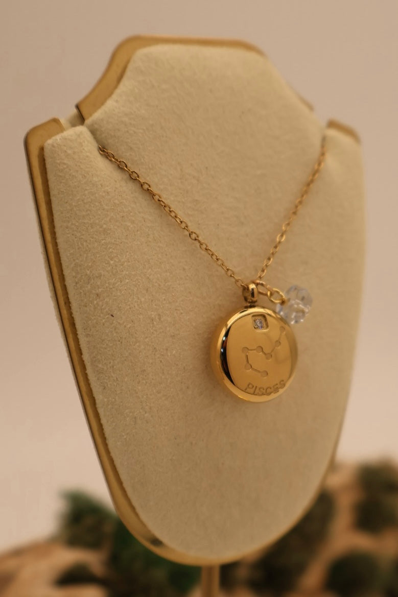 Gold necklace with a pendant on a beige display stand.