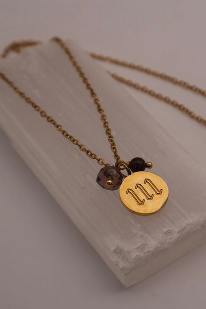 Gold necklace with a circular pendant and beads on a light wooden surface