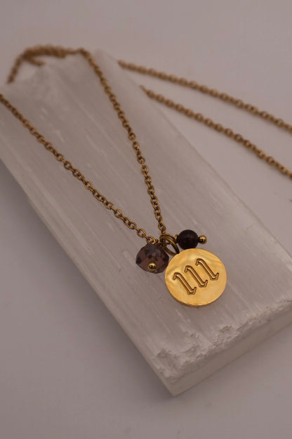 Gold necklace with a circular pendant on a white stone surface