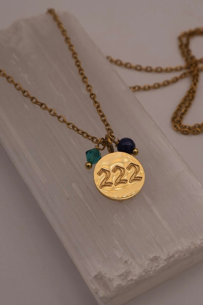 Gold necklace with a '222' pendant on a white stone surface