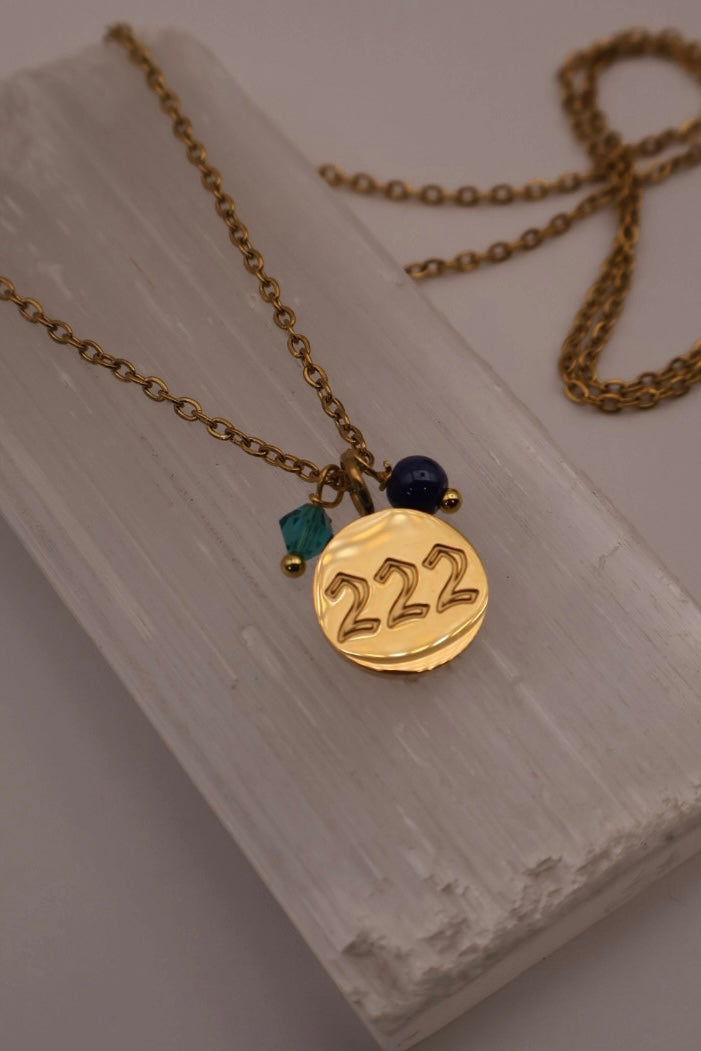 Gold necklace with '222' pendant on a white stone surface