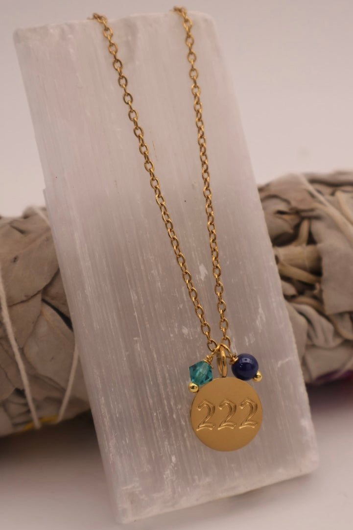 Gold necklace with a '222' pendant on a white stone surface
