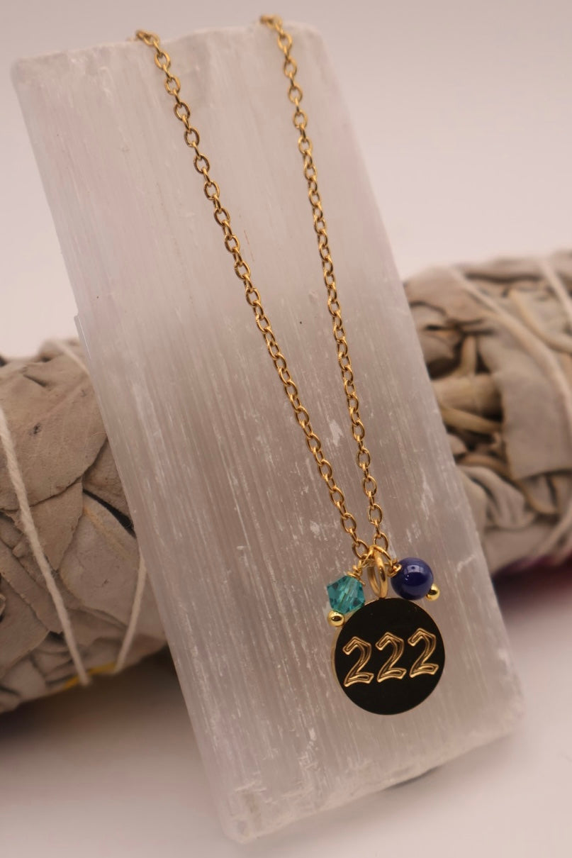 Necklace with a black pendant featuring the number 222, displayed on a white stone surface.
