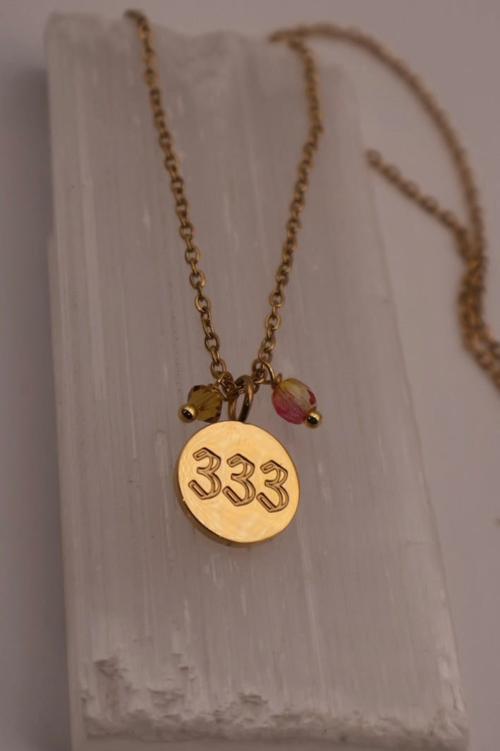 Gold necklace with a pendant displaying the number 333 on a light background