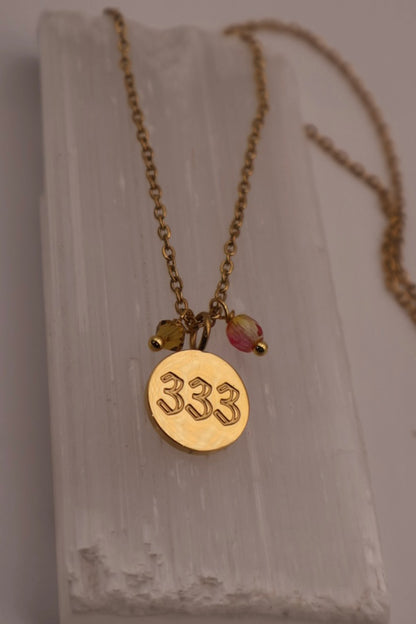 Gold necklace with a pendant displaying the number 333 on a light background