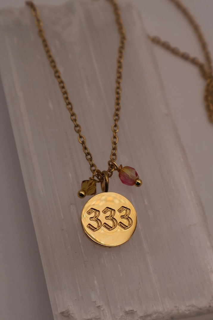 Gold necklace with a '333' pendant on a light wooden surface