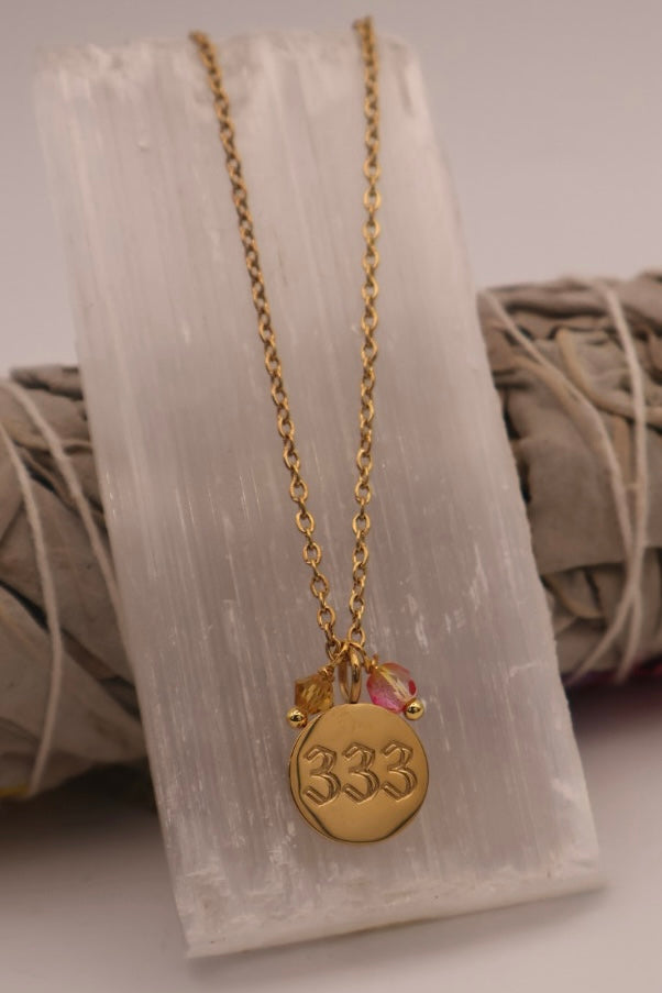 Gold necklace with a '333' pendant on a white stone surface