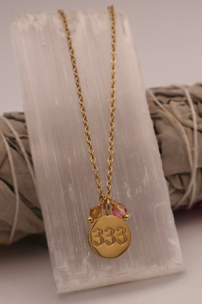 Gold necklace with a '333' pendant on a white stone surface