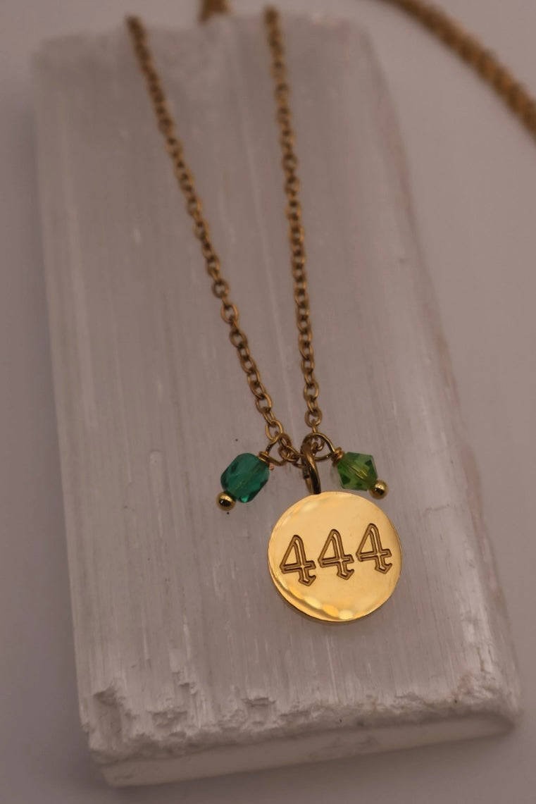 Gold necklace with a round pendant and green beads on a textured surface