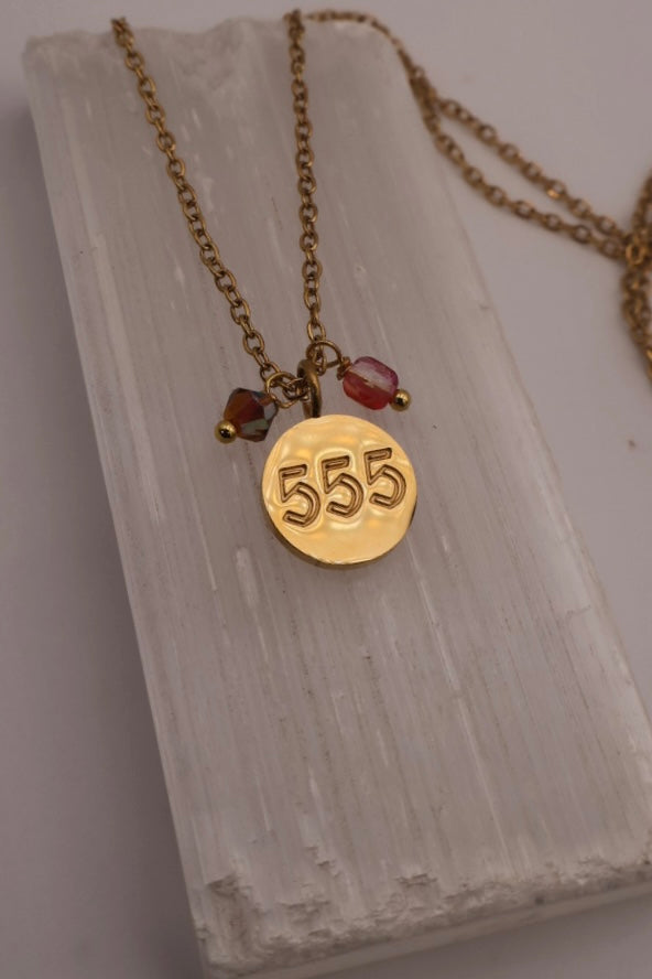 Gold necklace with a '555' pendant on a textured surface