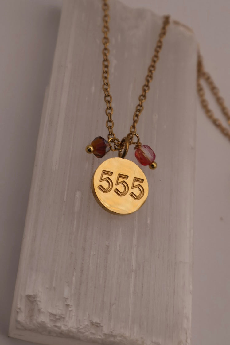 Gold necklace with a '555' pendant on a textured white surface