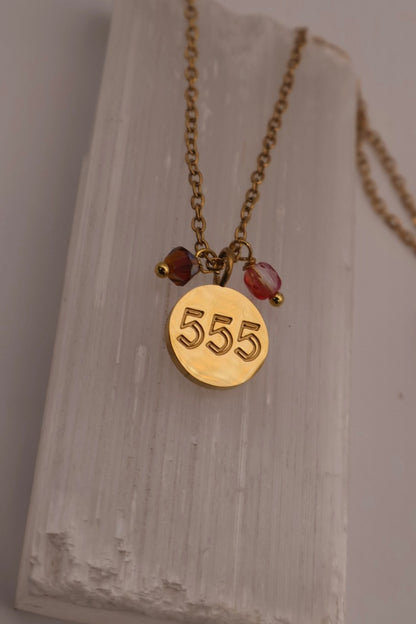 Gold necklace with a '555' pendant on a textured white surface