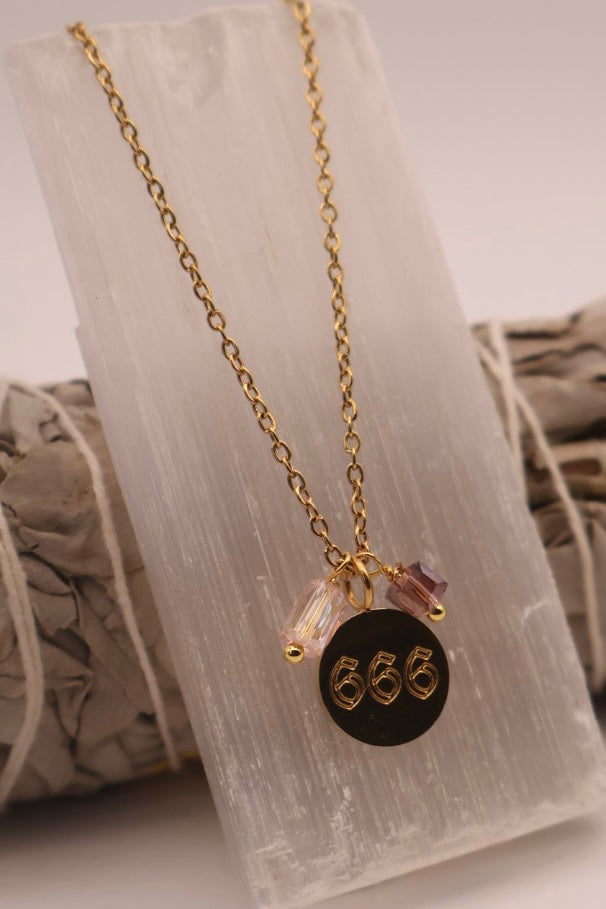 Gold necklace with a black pendant featuring the number '666' on a white background