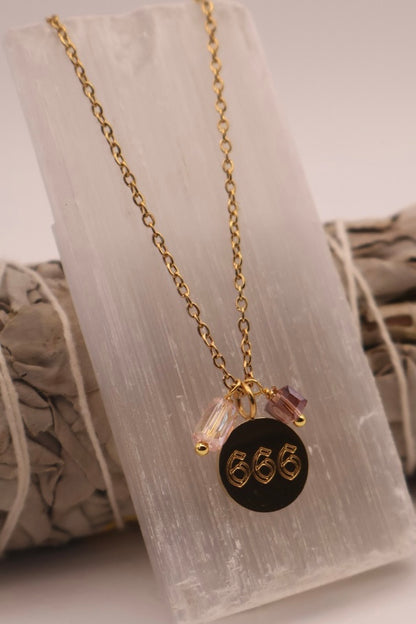 Gold necklace with a black pendant featuring the number '666' on a white background