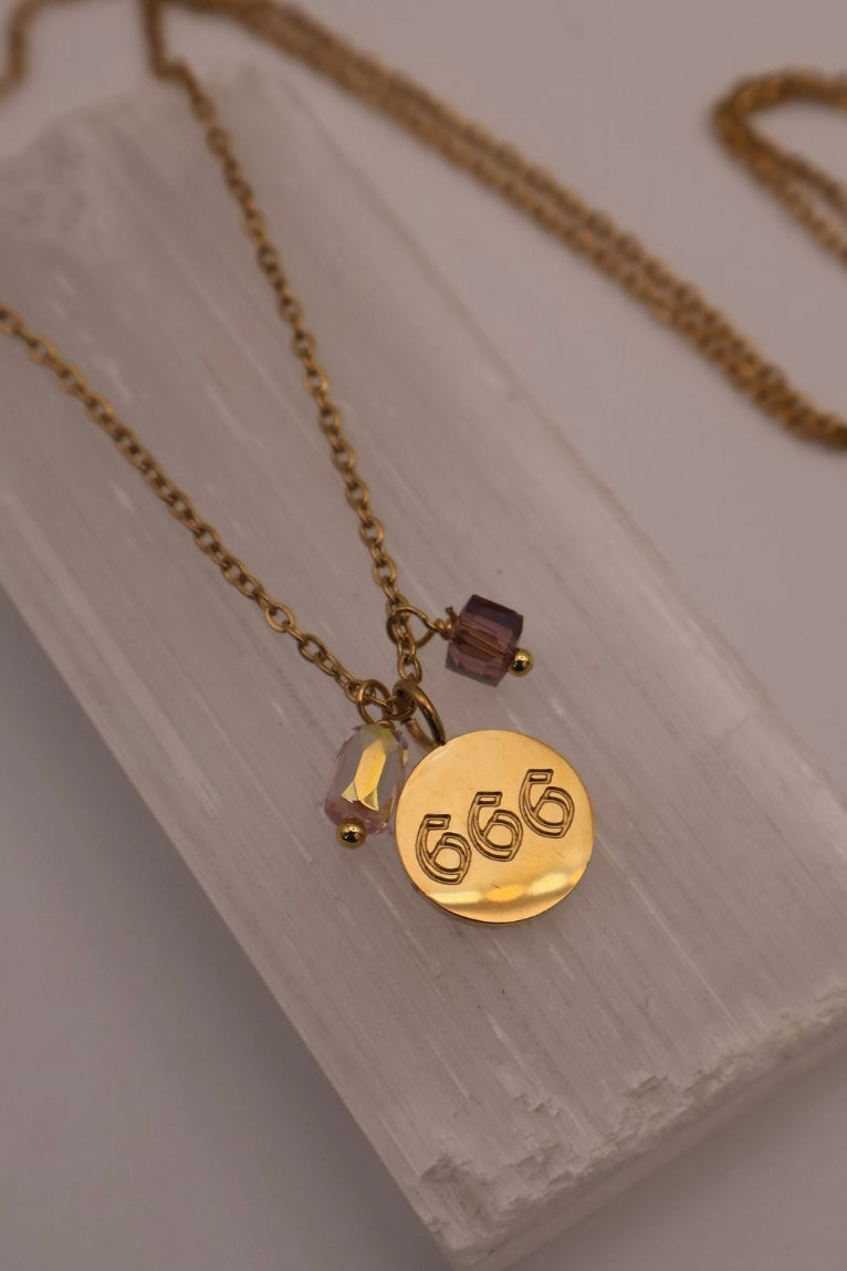 Gold necklace with a round pendant featuring the number '666' on a light wooden surface.