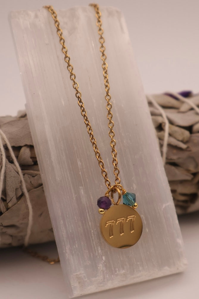 Gold necklace with a round pendant and colorful beads on a white stone surface