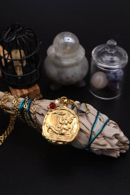 Gold pendant with blue cord on a smoldering sage stick against a dark background