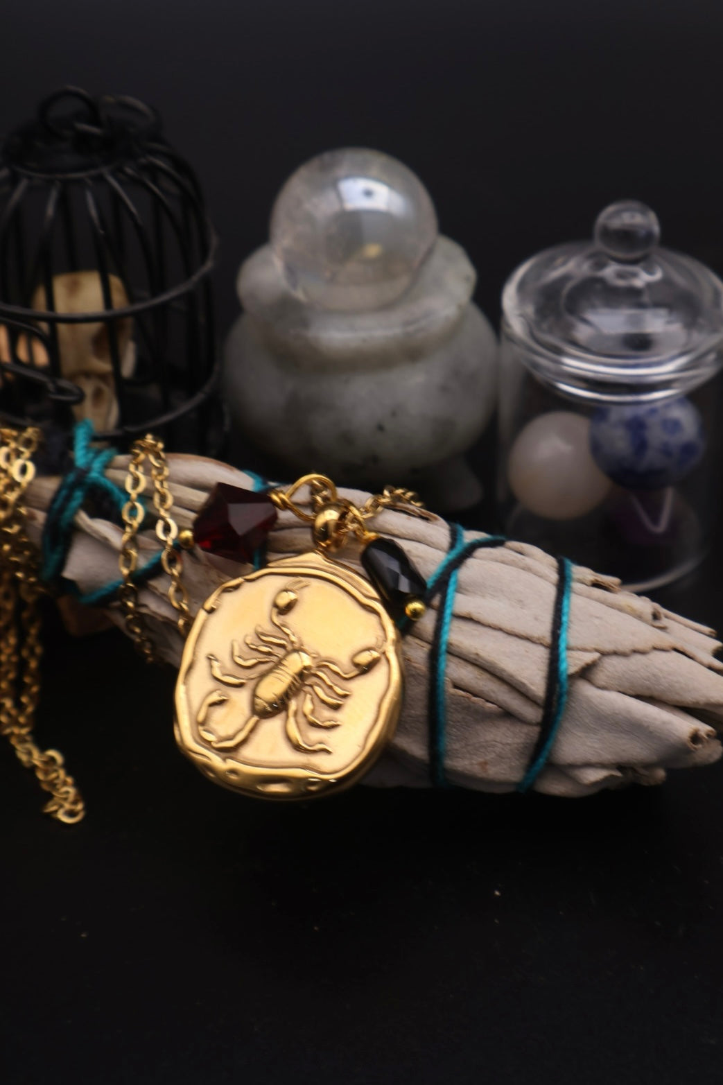 Gold scorpion pendant on sage with mystical items on a dark background