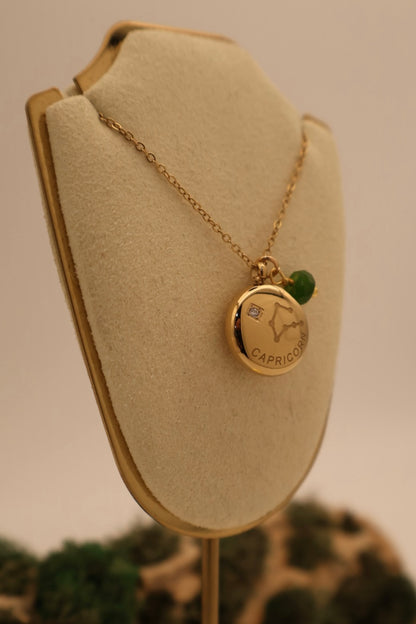 Gold necklace with a pendant on a beige display stand.