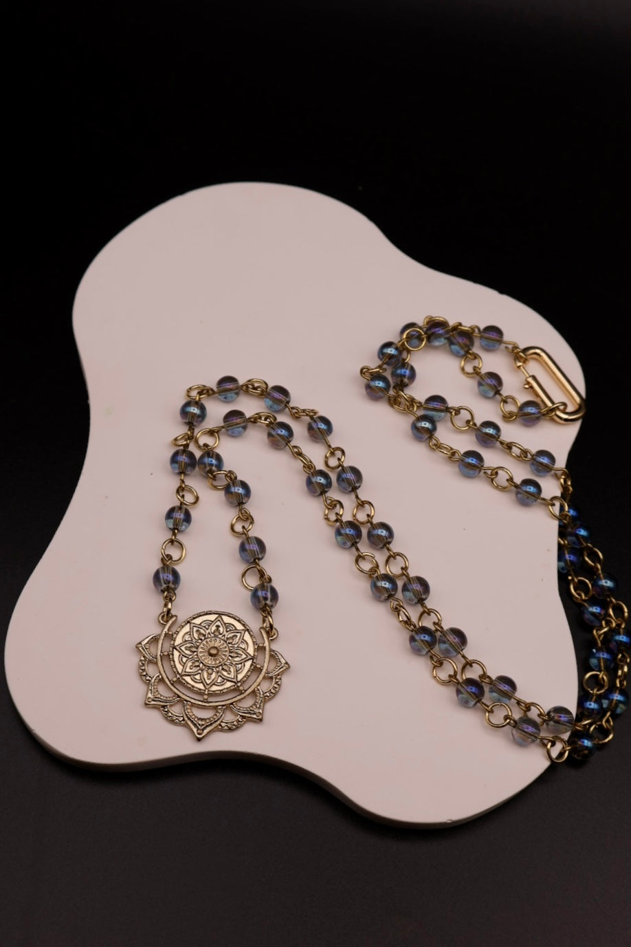 Necklace with blue beads and gold accents on a white stand against a black background