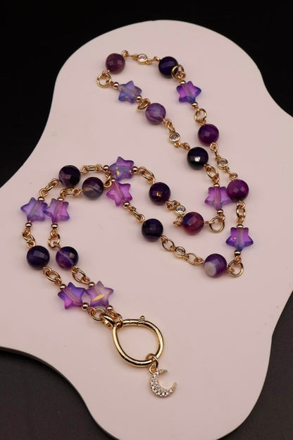 Necklace with purple beads and star-shaped charms on a white stand.