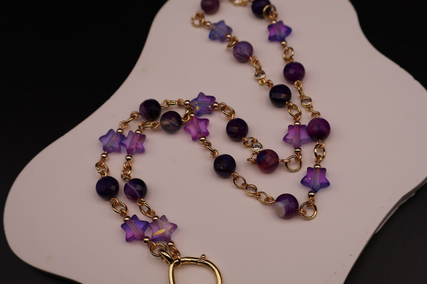 Purple beaded necklace with gold accents on a white stand
