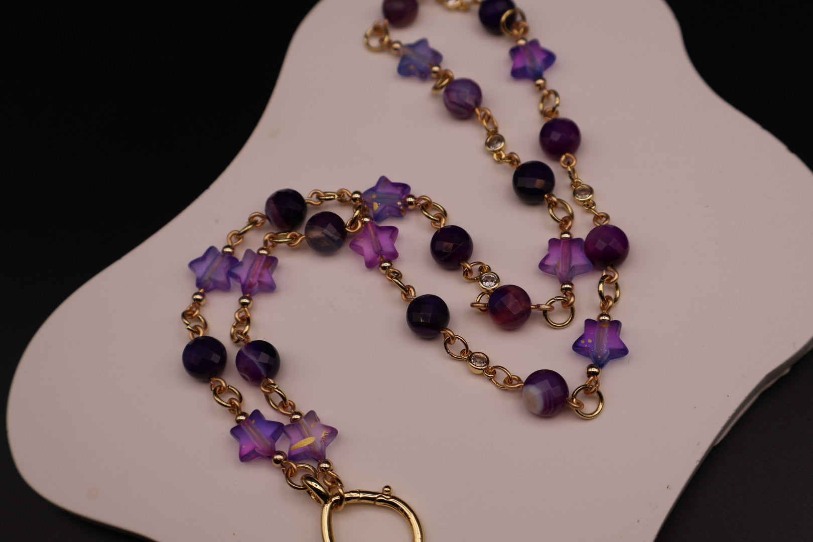 Purple beaded necklace with gold accents on a white stand