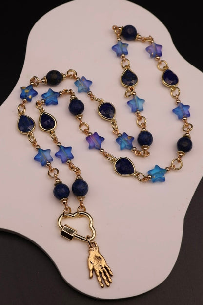 Necklace with blue star-shaped beads and gold hand charm on a white display stand.