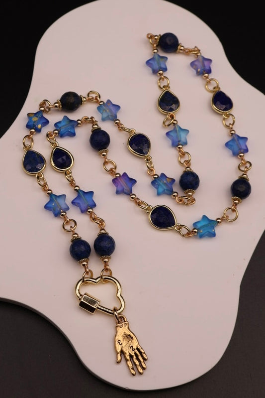 Necklace with blue star-shaped beads and gold hand charm on a white display stand.