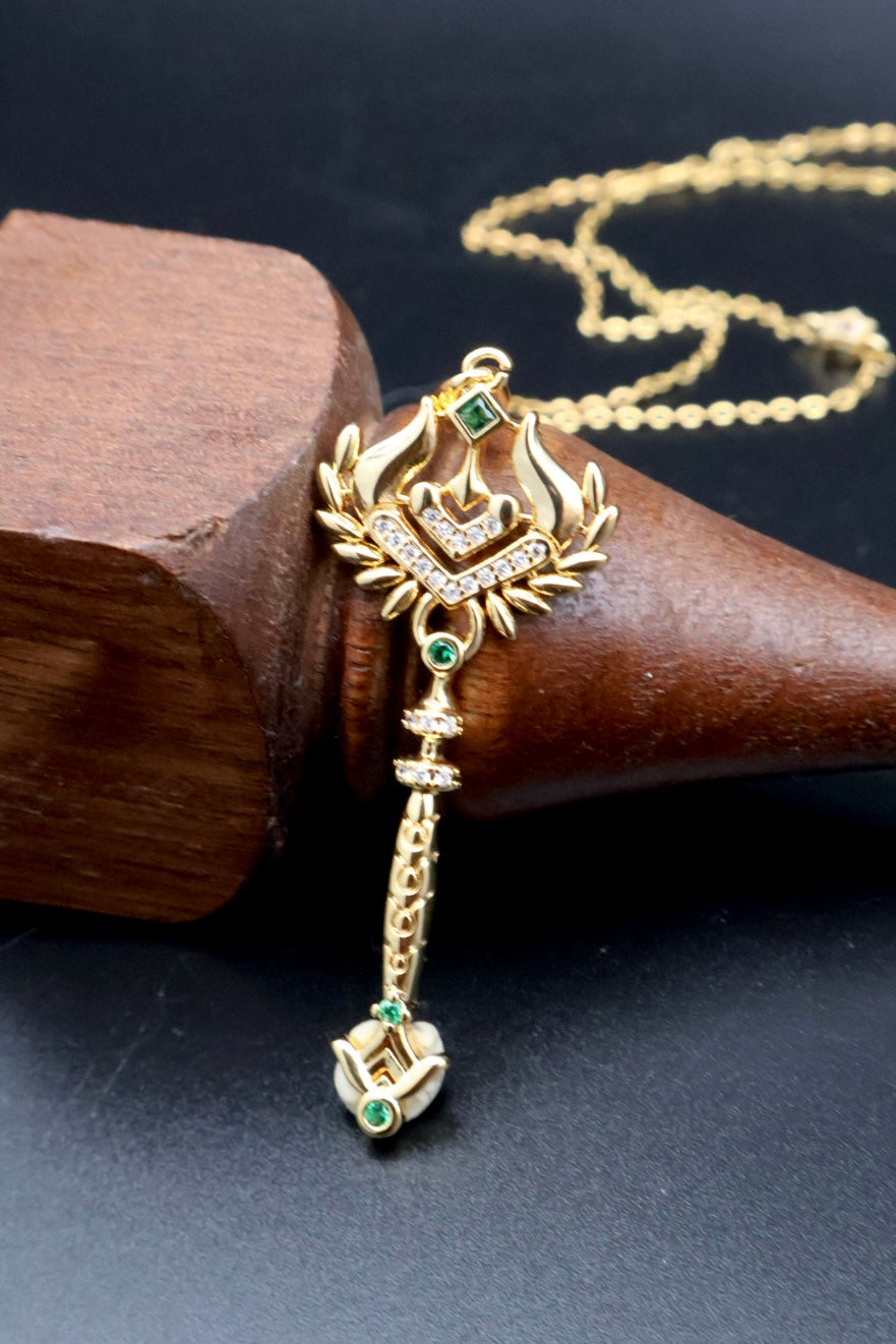 Gold-toned Indian style pendant necklace with a crown motif, green stone accents, and a dangling floral element, displayed on a dark wooden cone stand.