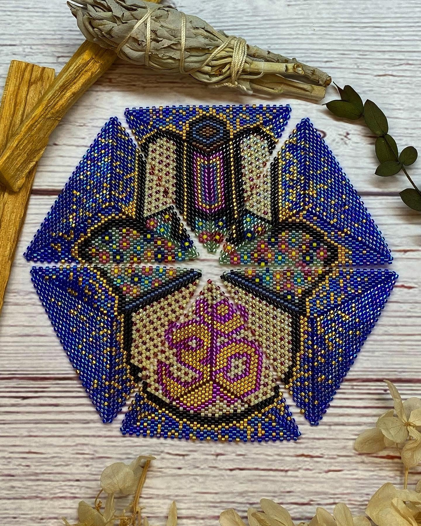 Hexagonal beaded coaster with geometric pattern on a wooden surface with leaves and sticks.
