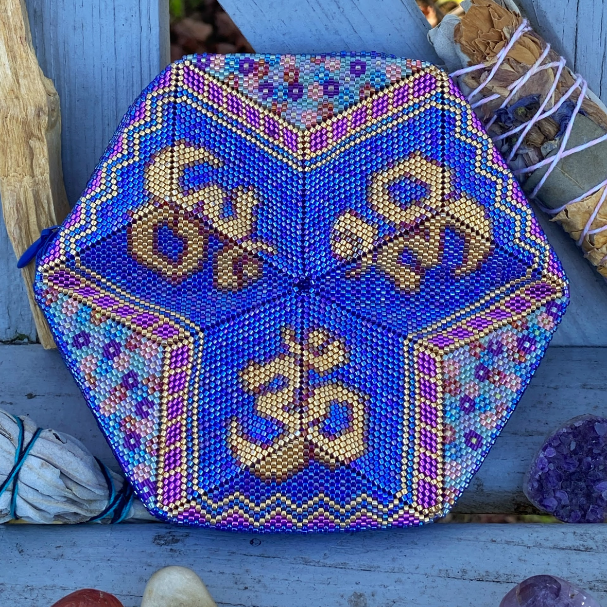Decorative hexagonal pouch with Om symbol on a wooden surface with stones and plants.