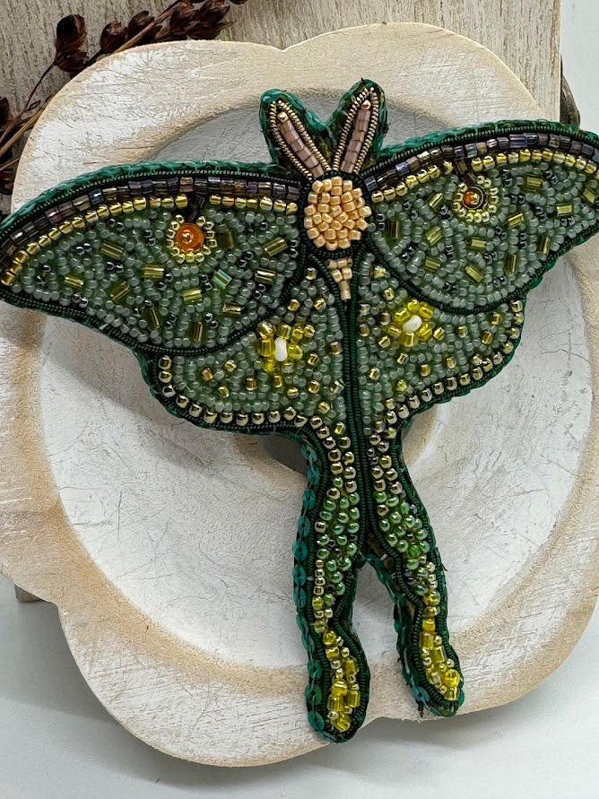 a closeup of a beaded luna moth pin with green beads of various shades