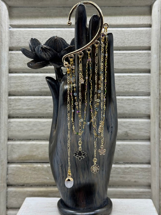 an ear cuff with gold chains and crystal beads on chains. there are various charms, a black lotus flower, gold charm, and gemstone charm