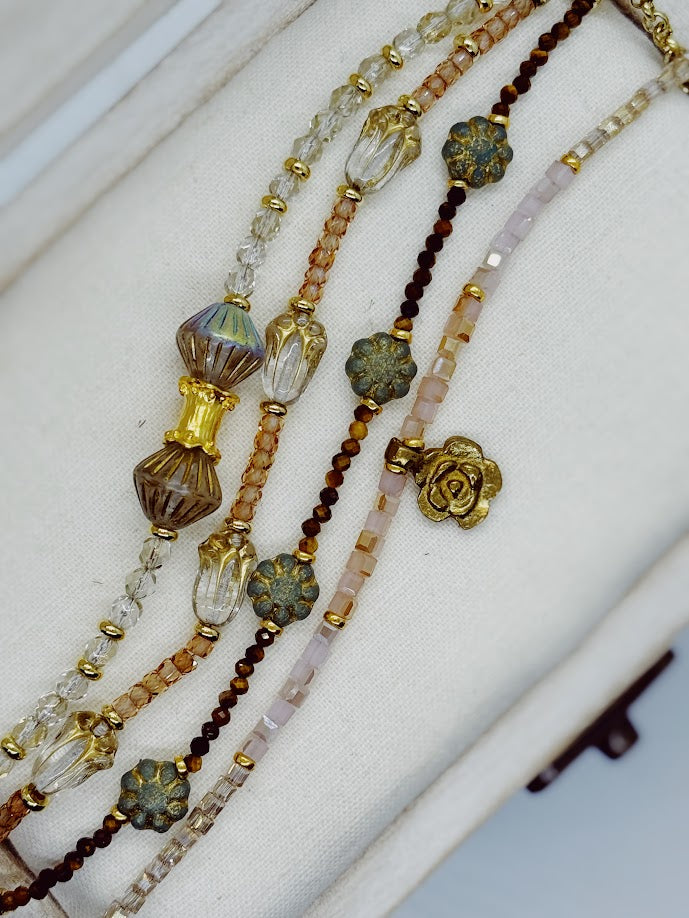 A bracelet with clear beads and baroque center beads, a bracelet with peach stones and clear tulip beads, a bracelet with tigers eye and green flowers, pink bracelet with a gold rose charm.