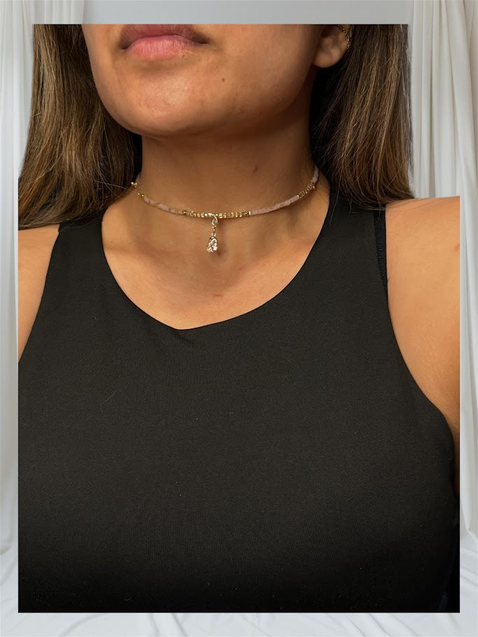 a woman wearing a round choker with pink beads of various shades and a gold tulip charm. the choker has gold accents.