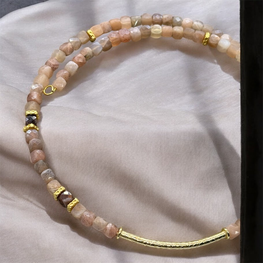 A close up of a choker made up of sunstone beads with gold accents. There is a gold bar as the center pendant for the choker