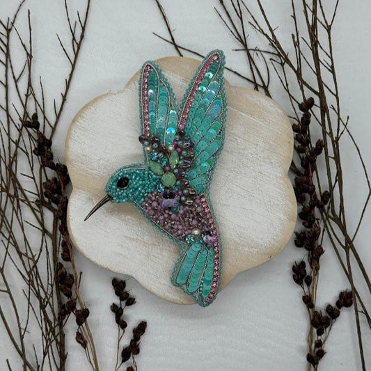 A teal hummingbird pin made of beads and sequins.