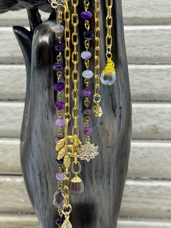 A closeup of the charms on the ear hanger showing a lotus charm, two cz charms, and two purple colored charms.