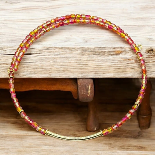 a choker with pink and yellow beads leaning on a block of wood.