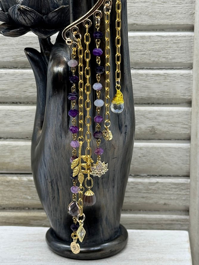 A closeup of the charms on the ear hanger showing a lotus charm, two cz charms, and two purple colored charms.